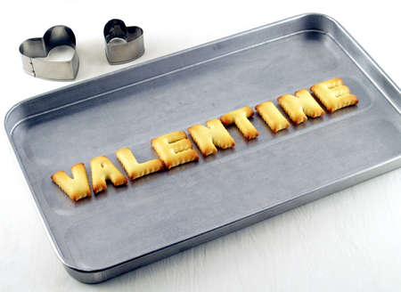 valentine word, biscuit cookies letters on oven tray with heart shaped cookie cutter on white backgroundの写真素材