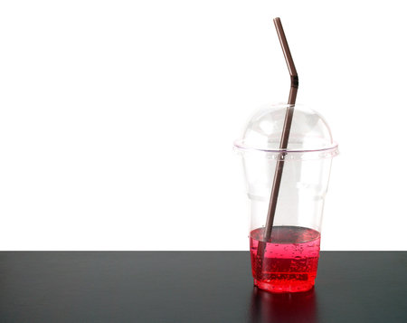 few red sweet drink with straw in transparent plastic cup on wooden table and white background