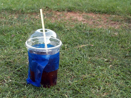 close-up soda pop in transparent plastic cup with white straw and blue bag on green grass field, cool refreshment carbonated drink and take away containerの写真素材