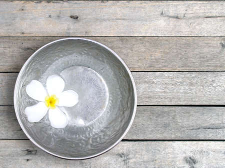 white frangipani (plumeria) flower floating on water surface in silver bowl on wooden decking floor, blooming flower and carved aluminum utensil for Songkran festival, top view with copy spaceの写真素材