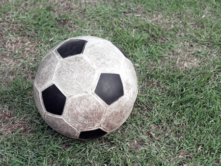 close-up old dirty stained soccer ball made of synthetic rubber on green grass field, sport item for outdoor sport exerciseの写真素材