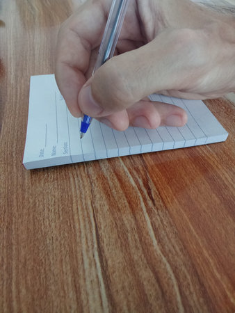 Man writing in a notebook with a pen on a wooden table.