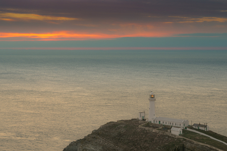 South Stack Lighthouse on the island of Anglesey in North Wales. The sun has set behind rain clouds and haze over the Irish Sea.の写真素材