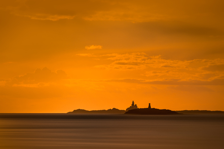 The Skerries Lighthouse and West Mouse, two famous landmarks on the North Wales coast, against the orange sky of an approaching sunset.の写真素材