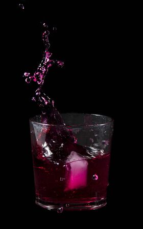 splash from ice cube in a glass of red water or drink isolated on a black backgroundの写真素材