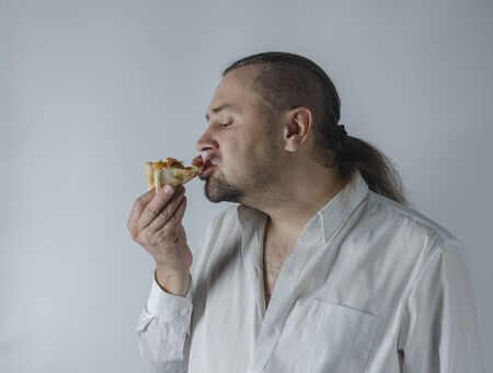 man with long hair in a white shirt eats a slice of pizzaの写真素材