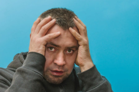 sad man holds his head on blue backgroung