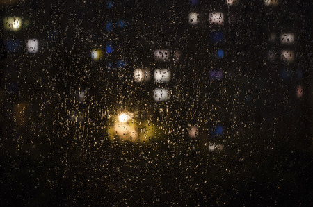 drops of rain on the window on the background of the night bokeh. Emotional melancholic abstract background with defocused lights. Focus on few drops due to the shallow depth of fieldの写真素材