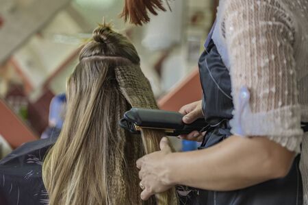 Hands of a hairdresser doing a model hairstyle for a girl, closeup back view. The concept for hairdressers. Girl in a hairdressing chair. Girl customer gets a hairstyle.の写真素材