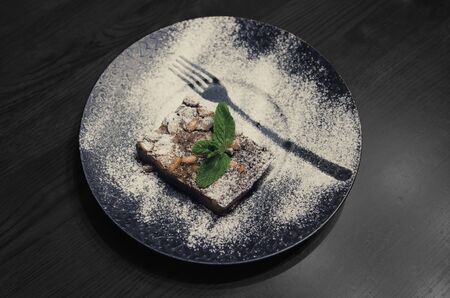 Chocolate dessert with nuts on a big black plate. finely decorated dessert on dark wooden tableの写真素材