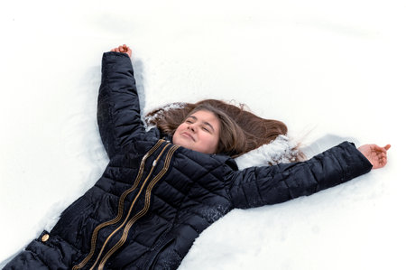 Teen girl lying on the snow and making a snow angelの写真素材