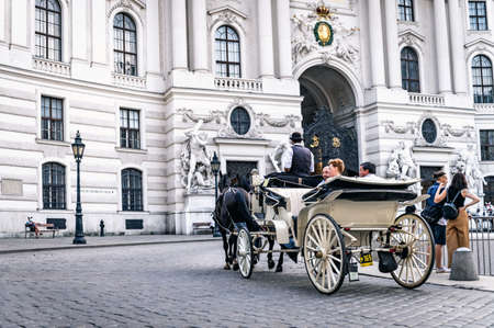 VIENNA, AUSTRIA - AUGUST 27, 2019. Horse carriage on a Vienna street passing by the Hofburg palace at Michaelerplatz with tourists and peopleのeditorial素材