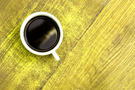 White cup of coffee on a yellow table. View from aboveの写真素材