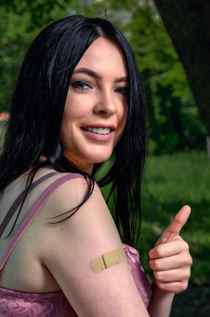 Smiling female with bandage on arm after vaccination .. Woman feeling positive after getting...