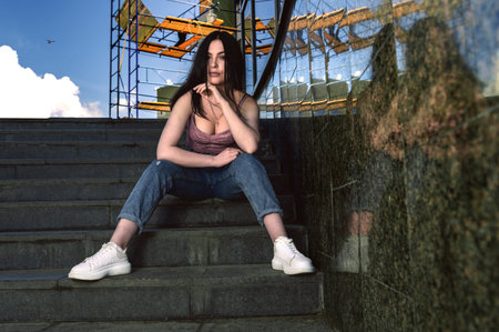Portrait of a young woman sitting on the steps outdoors. Pretty teenage girl in jeans