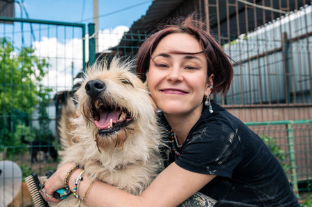 Dog at the shelter. Animal shelter volunteer feeding the dogs. Lonely dogs in cage with cheerful woman volunteerの写真素材