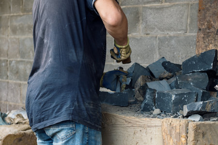 Man working with hard stone with hammer and chisel. Stonemason splits basalt stonesの写真素材
