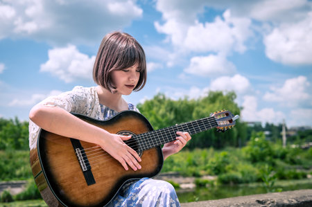 Teenage girl play guitar outdoor. Teenage girl with a guitar. Portrait of a girl playing the guitarの写真素材