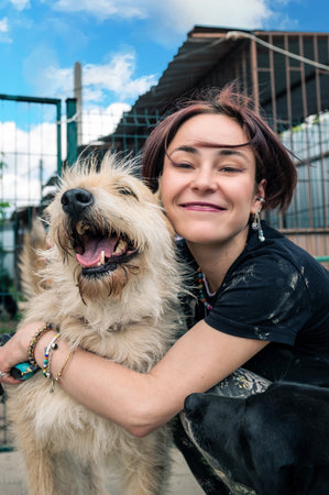 Dog at the shelter. Animal shelter volunteer takes care of dogs. Lonely dogs in cage with cheerful woman volunteer. vertical imageの写真素材