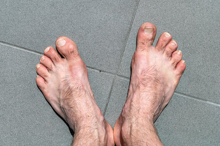 Bare legs of a man. Naked male legs on tile floor with copy space. Male bare feet, toes with long...