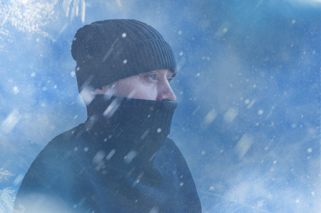 Frozen man shivering from cold weather on a blue snowy background. Man trying to warm himself up during a winter coldの写真素材