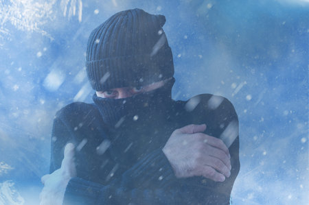 Frozen man shivering from cold weather on a blue snowy background. Man trying to warm himself up during a winter coldの写真素材