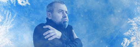 Frozen man. shivering from cold weather on a blue snowy background. Man trying to warm himself up during a winter cold. Banner designの写真素材