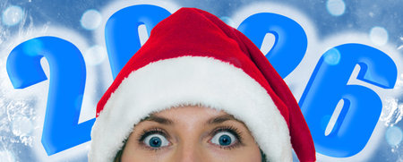 Young woman wearing a Santa hat on frozen blue background. 2026 inscription. Girl celebrating...