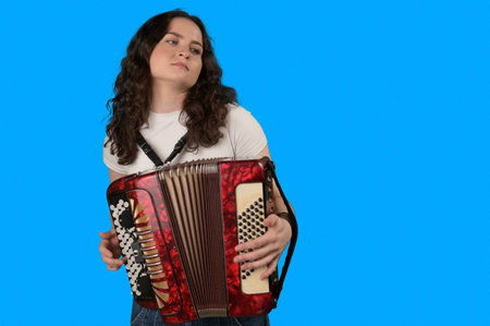 Young woman with a button accordion. Adult woman plays the button accordion on blue backgroundの写真素材