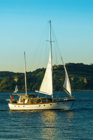 Sailboat with a white sail. Sailboat glides through calm waters off the coast against a backdrop of...
