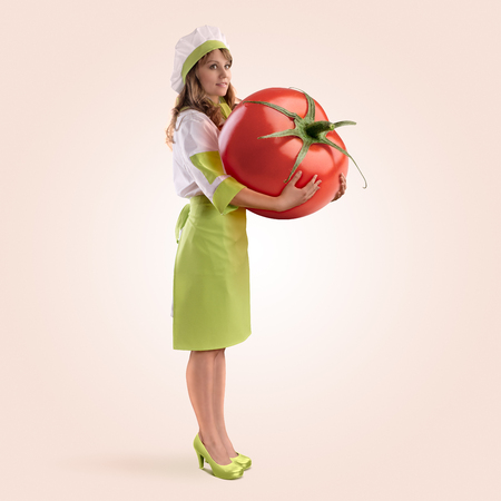 cook girl holding a large tomato on a beige backgroundの写真素材
