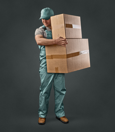 delivery man in green uniform holding a box on a gray backgroundの写真素材