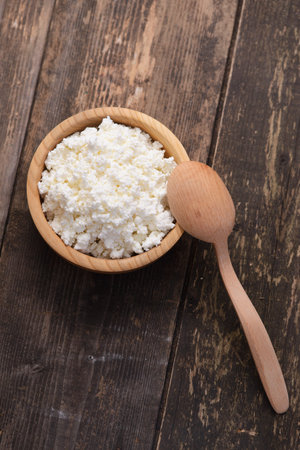 curds in a wooden bowl on a dark wooden background
