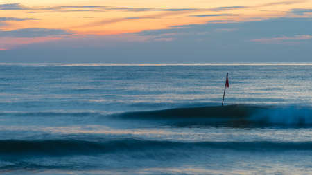 two waves an a red flag at morningの写真素材