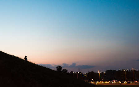 A boy with a mobile phone walks up a hill in the a city at eveningの写真素材