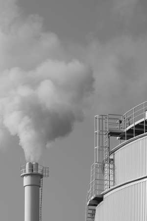 A smoking chimney next to a silo in black and whiteの写真素材