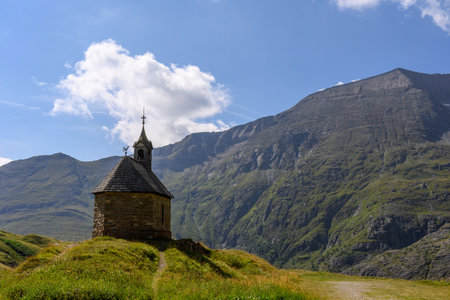 Old chapel on a green hill in front of an alpine panoramaの写真素材