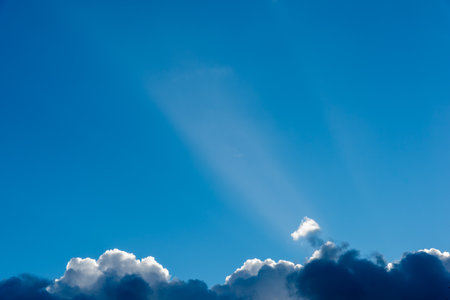 Sunbeams in the blue sky above fluffy cloudsの写真素材
