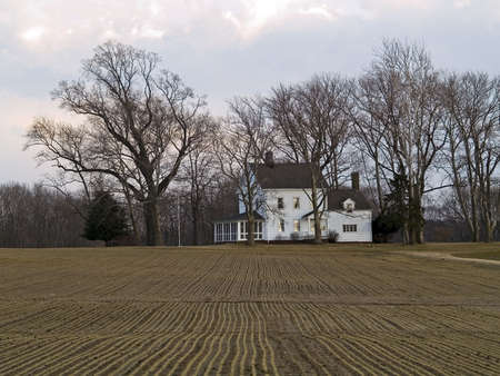 A white farmhouse framed by  winter trees and the  rows of a field.の写真素材