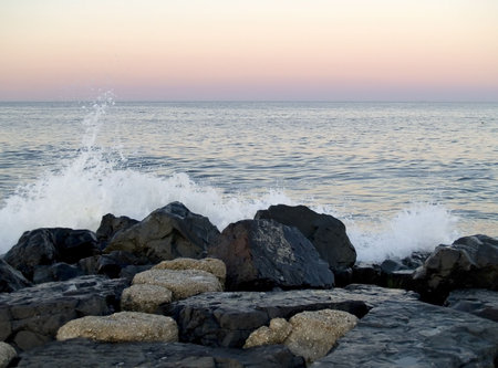 A wave crashes over a jetty along the New Jersey shore at sunset