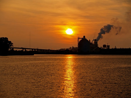 The sun sets along the Georgetown River in South Carolina with industrial buildings in the...
