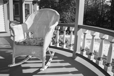 A wicker rocking chair on a porch in black and white.の写真素材