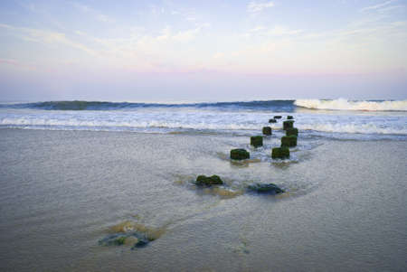 The surf over an old jetty along the beach in Belmar, New Jersey at sunset.の写真素材