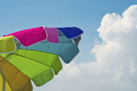 A colorful beach umbrella contrasted against a blue sky.の写真素材