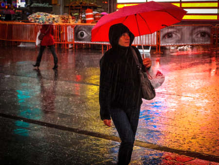 A lady with a red umbrella walks through Times Square on April 16 2014 のeditorial素材