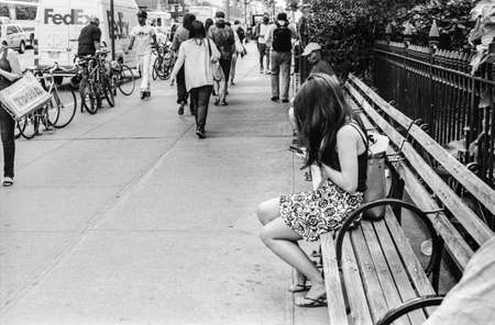 A b w film photograph of a girl with long black hair texting on a park bench outside Madison Park in Manhattan のeditorial素材