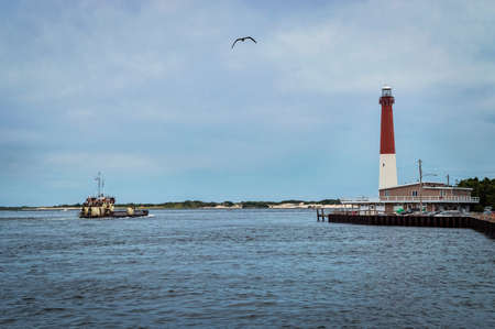 A fishing boat sails past the Barnegat Lighthouse on Barnegat Bay in Ocean County New Jersey.の写真素材