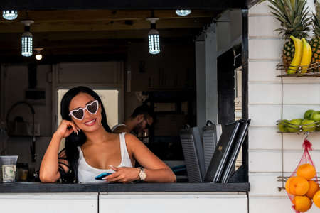 PHILLIPSBURG, ST. MAARTEN - JULY 11 - An attractive young woman with heart shaped sunglasses sells fruit shakes on the boardwalk  on July 11 2018 in Phillipsburg, St. Maarten.のeditorial素材