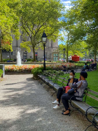 NEW YORK-SEPTEMBER 1: Women relax on a park bench wearing masks during Cover 19 in Bowling Green on September 1 2020 in lower Manhattan.のeditorial素材