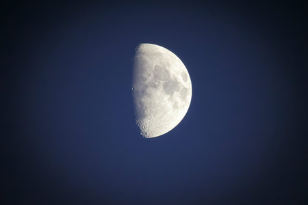 A telephoto view of the half moon in the evening sky.